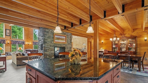 A spacious kitchen with a large island, stone fireplace, and wooden ceiling beams.