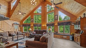 A spacious wooden cabin with high ceilings, large windows, and a cozy living area with a sofa and fireplace.