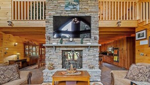 A cozy living room with a stone fireplace, wooden furniture, and a television mounted above the fireplace.