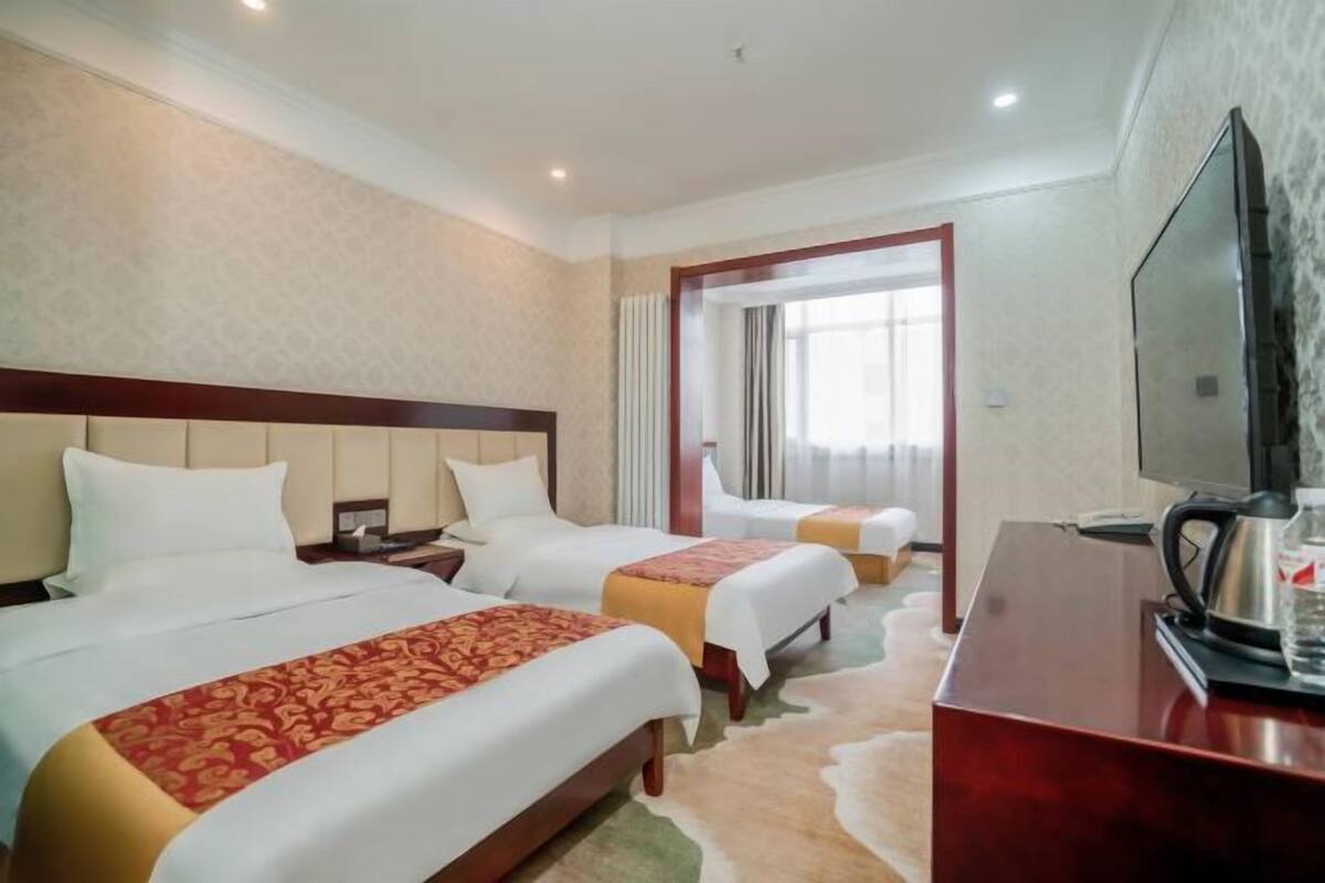 A hotel room with two beds, a TV, a desk, and a view of the outside through a window.