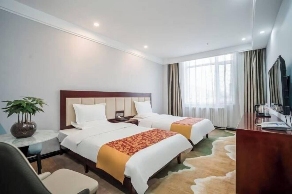 A hotel room with two beds, a desk, a chair, a television, and a window with curtains.