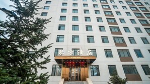 Entrada de un hotel con un letrero en idioma extranjero, una escalera que conduce a la entrada y un edificio alto al fondo.