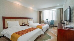 Habitación de hotel con dos camas, un escritorio, una silla, un televisor y un ventanal con cortinas.
