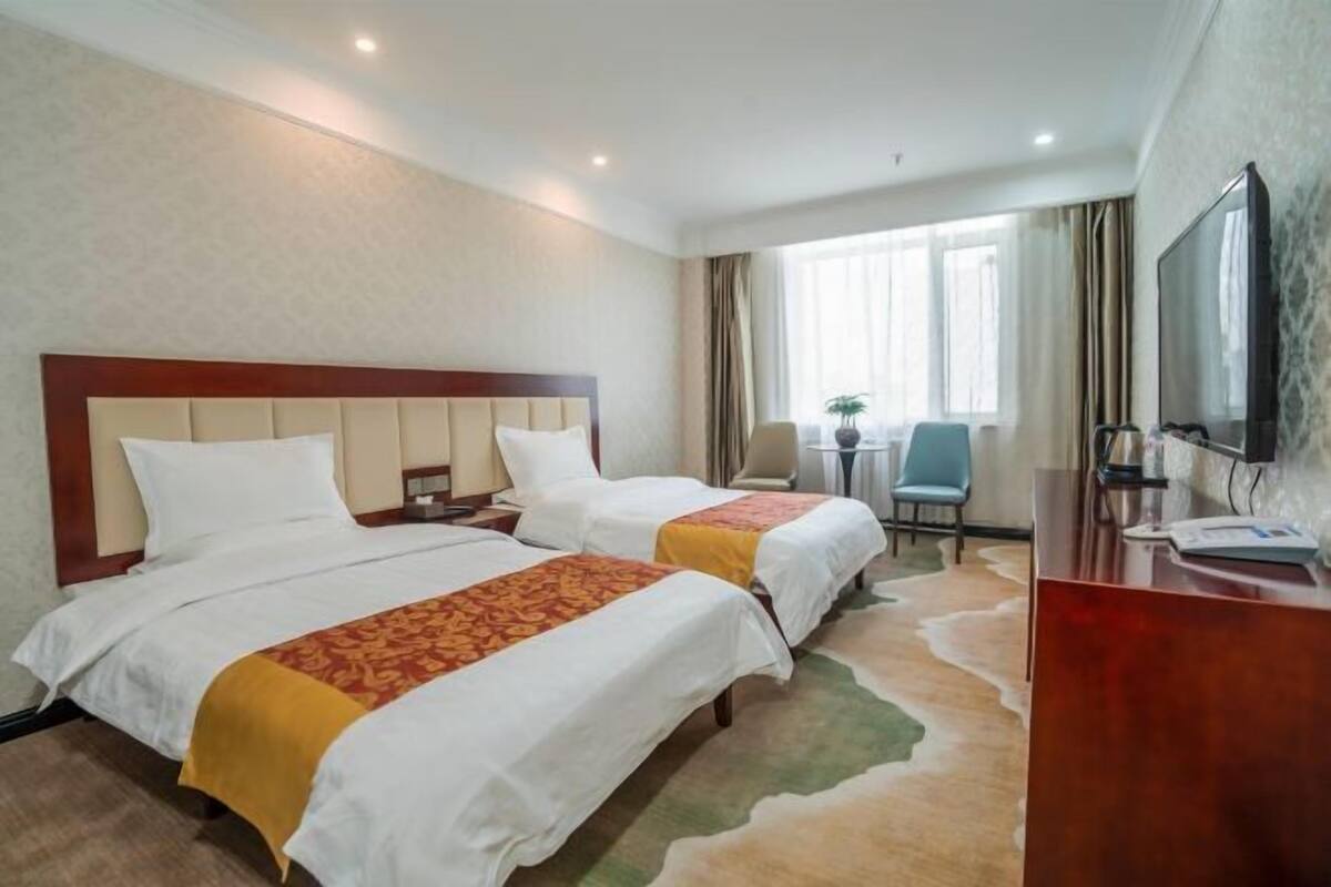 A hotel room with two beds, a desk, a chair, a TV, and a window with curtains.