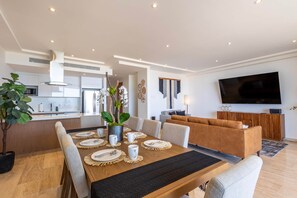Een moderne woonkamer met een eethoek, een bank, een televisie en een keuken op de achtergrond.