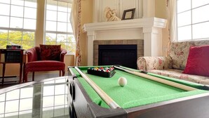 A billiards table in a room with a fireplace, a red armchair, and a sofa with floral upholstery.