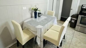 A dining area with a table covered in a protective sheet, four chairs, a vase with flowers, and a mug with text.