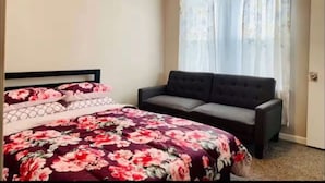 A bedroom with a bed, a sofa, and a window with curtains.