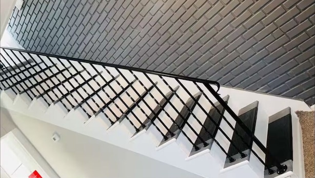 A modern staircase with a black metal railing, white walls, and a grey brick-patterned wall.