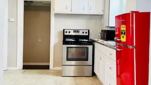 A kitchen with white cabinets, a stainless steel oven, a red refrigerator, and a tiled floor.