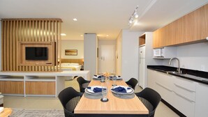 A modern kitchen with wooden cabinets, a built-in microwave, and a dining area with a wooden table set for four. - Sunset Lagoa  (Florianopolis)