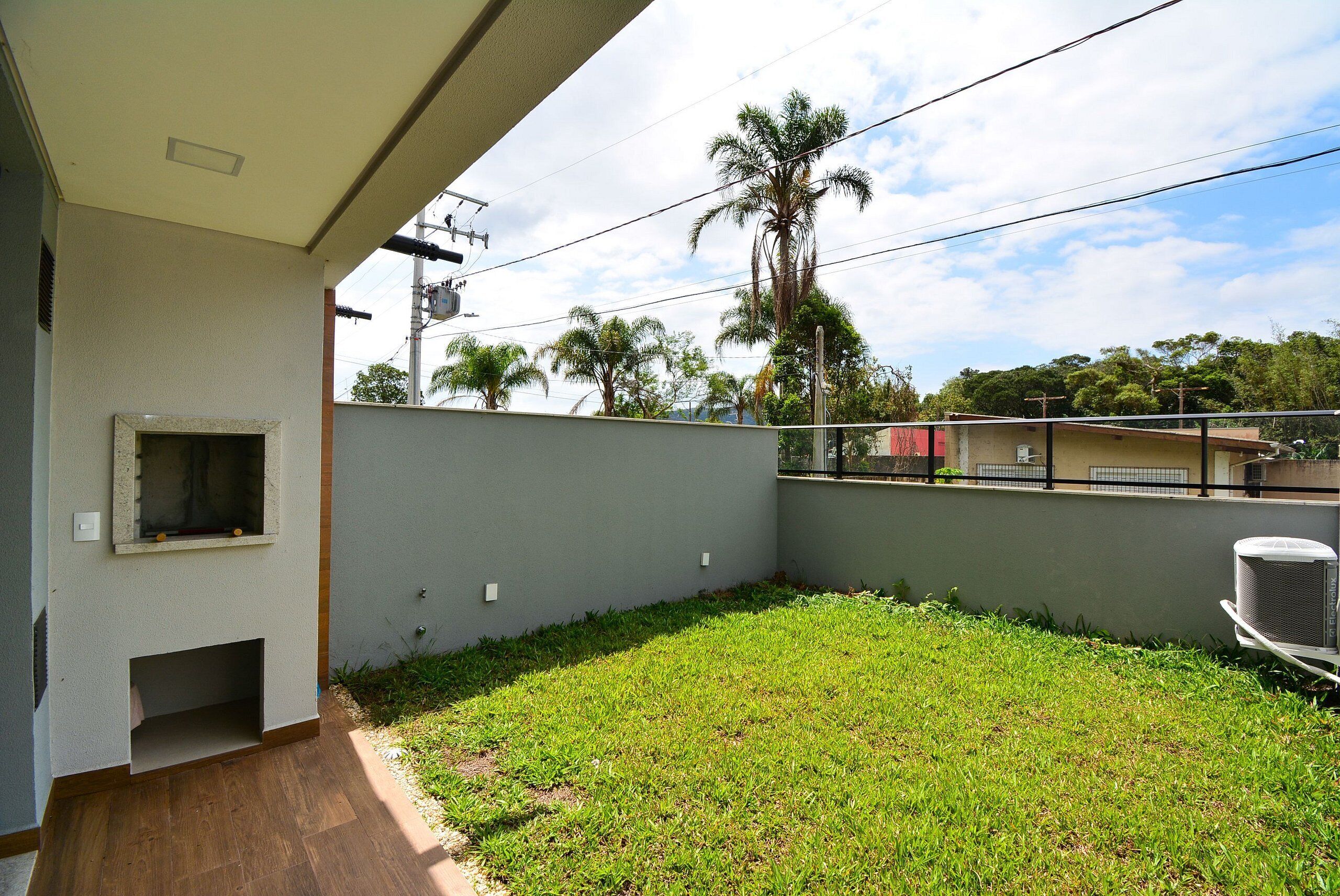 A balcony with a small enclosed area, a grassy yard, and a view of palm trees and buildings in the background.