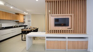 A modern kitchen with a built-in TV, white cabinetry, and a dining area with a table and chairs. - Sunset Lagoa  (Florianopolis)