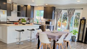 A modern kitchen with a central island, bar stools, and a dining table with chairs. - Homey Place in Sechelt , close to town and beaches (Sechelt)