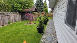 A backyard with a well-maintained lawn, potted plants, a wooden deck, and a small shed. - Homey Place in Sechelt , close to town and beaches (Sechelt)