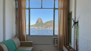 Une pièce dotée d’une grande fenêtre donnant sur un paysage montagneux et un port où sont amarrés des bateaux.