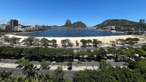 Un paysage urbain côtier avec une montagne imposante, une plage et un parking bordé d’arbres.