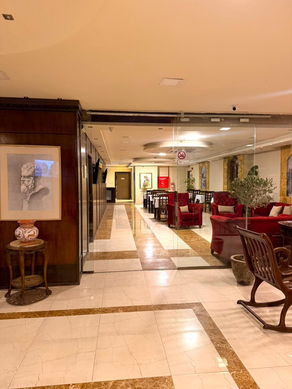 Recepció d'hotel amb taulell d'entrada, zona d'estar amb sofàs vermells, sòl de rajola i una obra d'art emmarcada a la paret.