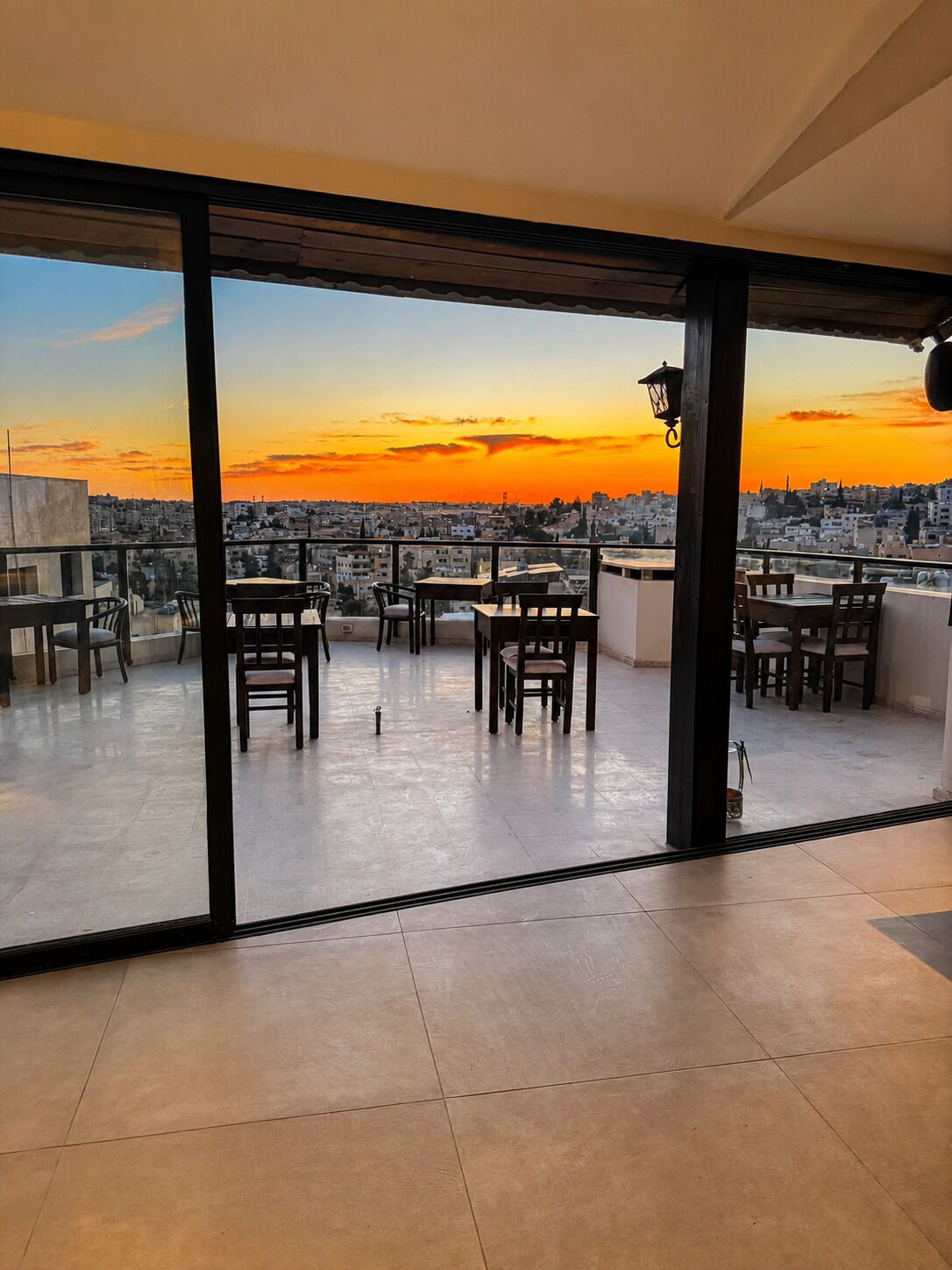 Une terrasse sur le toit, aménagée avec des tables et des chaises, offrant une vue sur la ville au coucher du soleil.