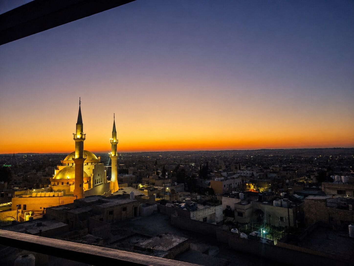 A cityscape at dusk with prominent mosque architecture, including domes and minarets, and a view of the surrounding urban area.