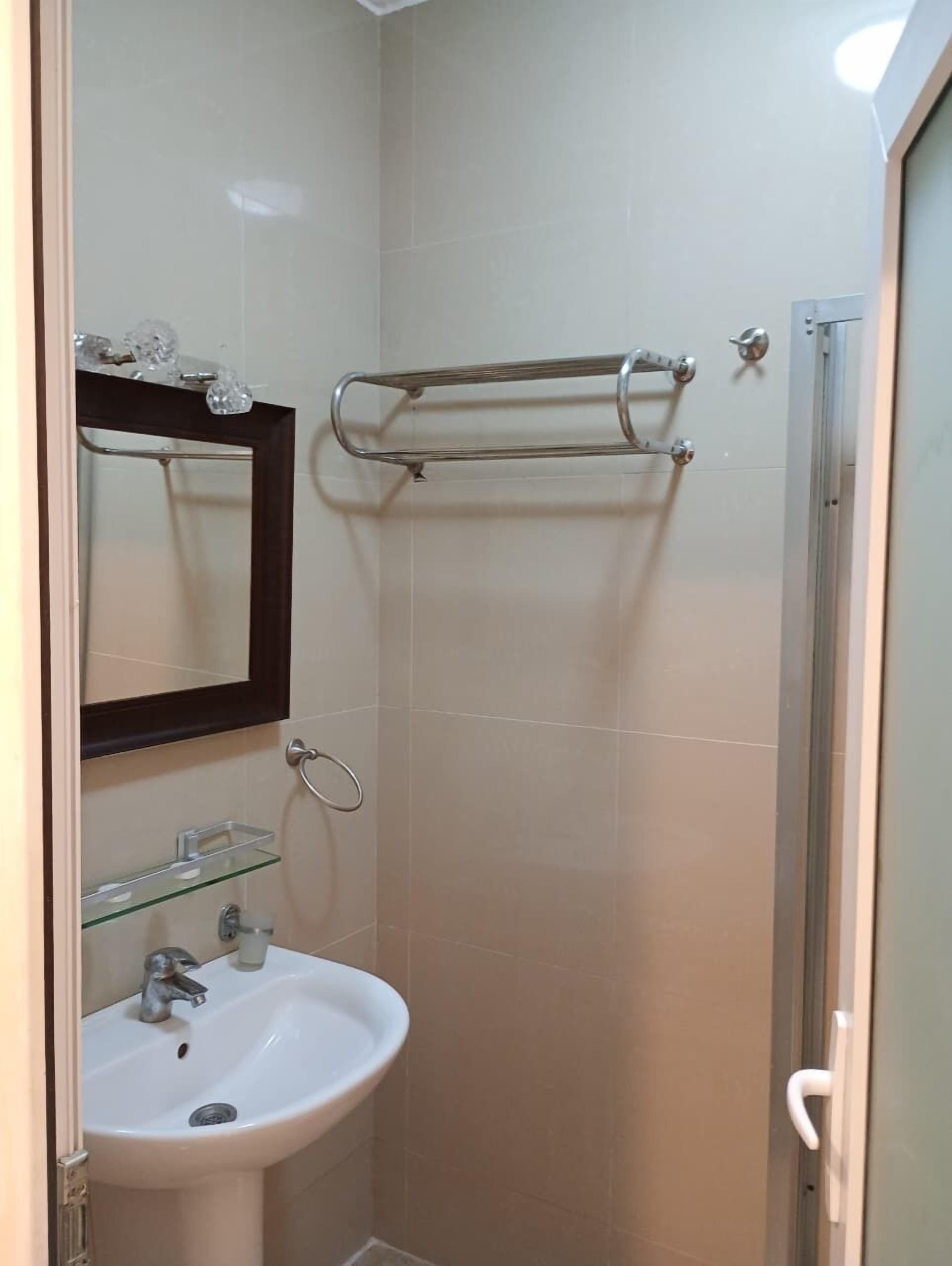 Un baño con lavamanos blanco, repisa de vidrio, toallero y espejo.