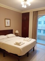 Habitación de hotel con una cama grande, una mesita de noche, una lámpara, un armario y vistas al exterior.