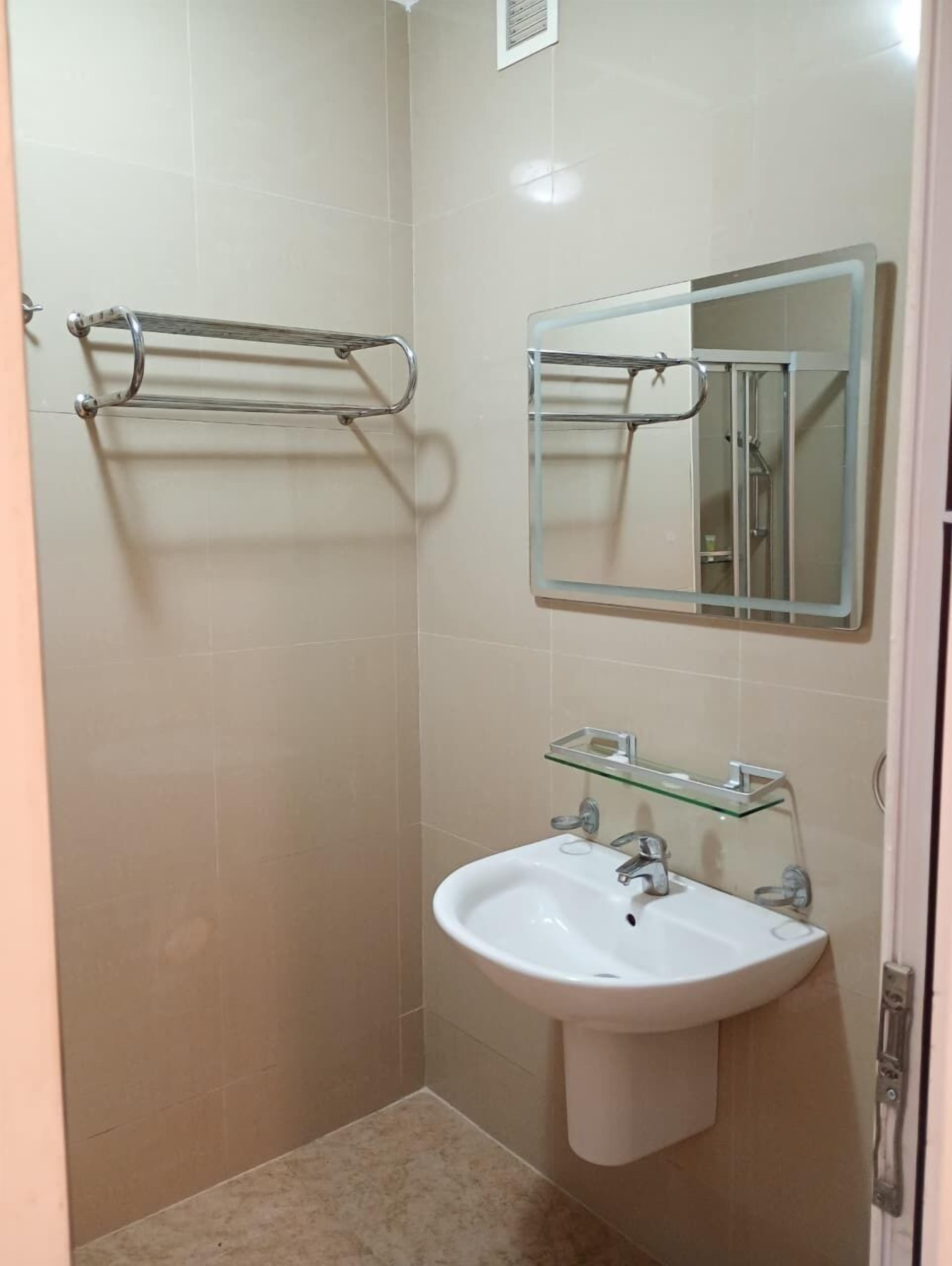 A small, modern bathroom with a white sink, a glass shelf, a towel rack, and a mirror.