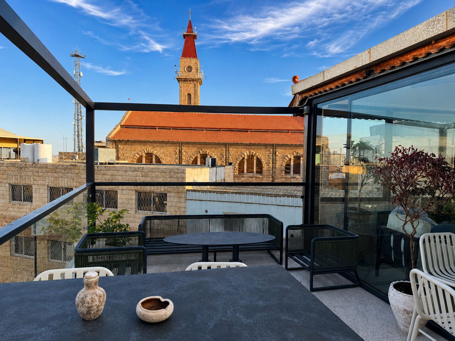 Een terras met een tafel en stoelen, met uitzicht op een historisch gebouw met een rood dak en een toren.