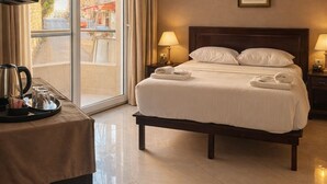 Quarto de hotel com uma cama, abajures, televisão e vista da rua através de uma janela grande.