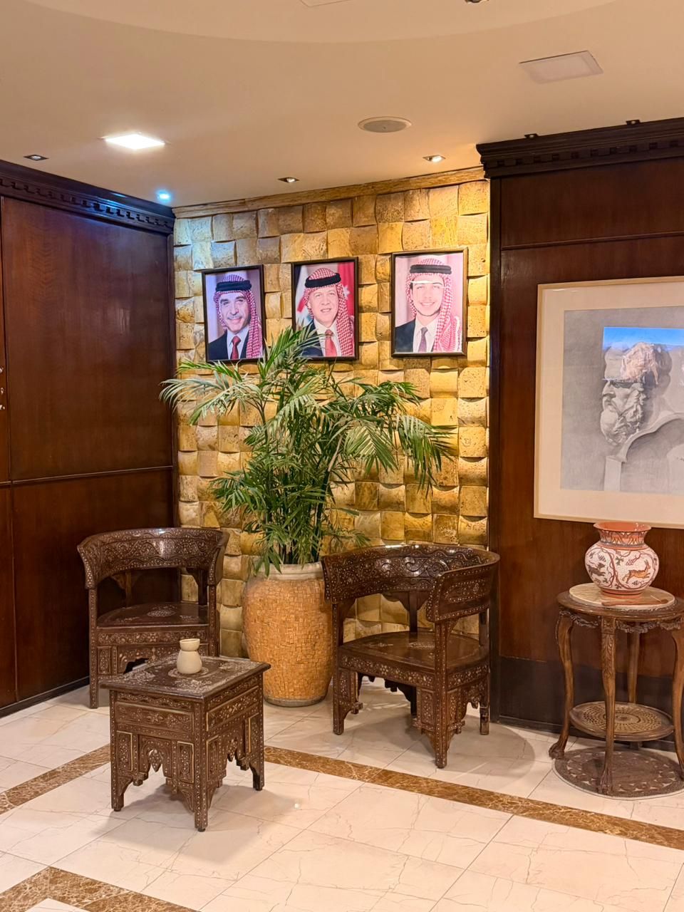 Un vestíbulo con pared de piedra, retratos enmarcados, una planta grande en maceta y muebles de madera tradicionales.