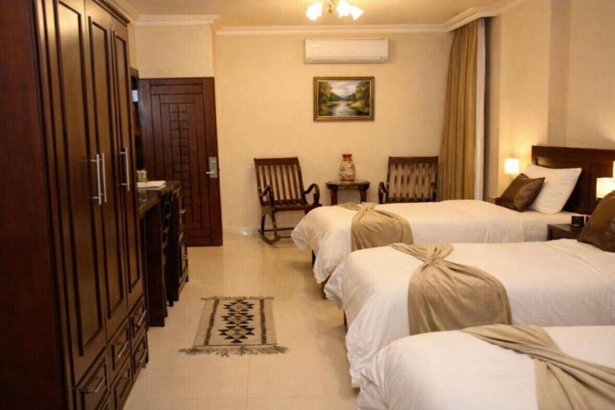 A hotel room with two beds, a wardrobe, a painting on the wall, and a small table with chairs.