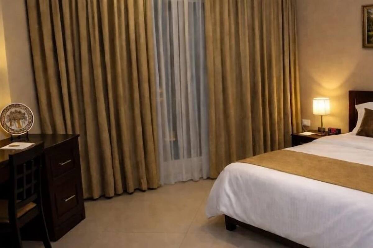 A hotel room with a bed, a nightstand, a lamp, and a painting on the wall.