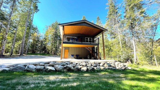 A two-story cabin with a stone foundation, surrounded by a forest.