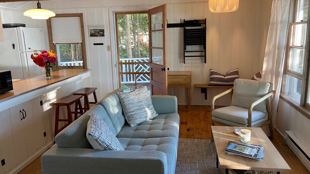 Un salon confortable avec un canapé, une table basse et un fauteuil. Il y a également un coin cuisine équipé d’un réfrigérateur et d’un four à micro-ondes. Une porte en bois donne accès à un espace extérieur.