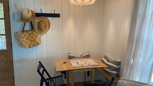 Une pièce d’angle avec une table en bois, des coussins à rayures, un chapeau et un sac en fibres tressées accroché au mur.