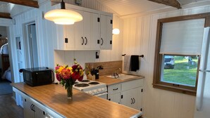 Une cuisine avec des meubles blancs, un plan de travail en bois, une cuisinière, un évier et une fenêtre donnant sur l’extérieur.