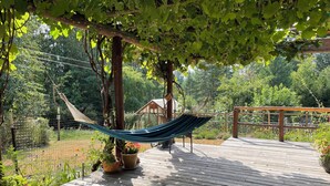 A wooden deck with a hammock, potted plants, and a wooden bench. - Charming 1-bedroom apartment in a beautiful natural setting, minutes from town. (Sandpoint)