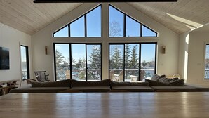 A spacious room with a large wooden table and chairs, a built-in bench with cushions, and large windows offering a view of snow-covered trees and a deck.