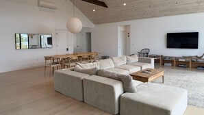 A spacious living room with a large sectional sofa, a wooden coffee table, and a dining area with a long table and chairs.