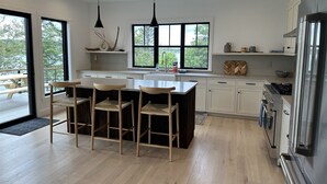 A modern kitchen with a large island, wooden chairs, a sink, and a stove.