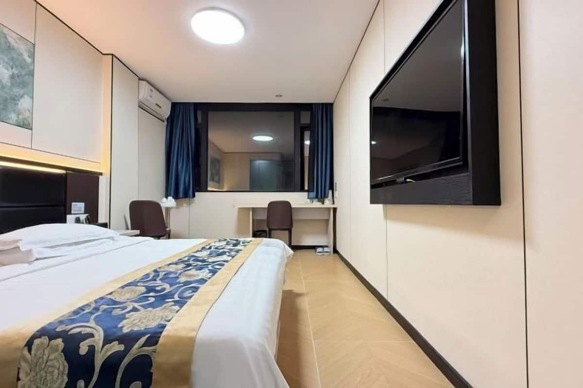 A hotel room with a bed, desk, chair, TV, and a large mirror.