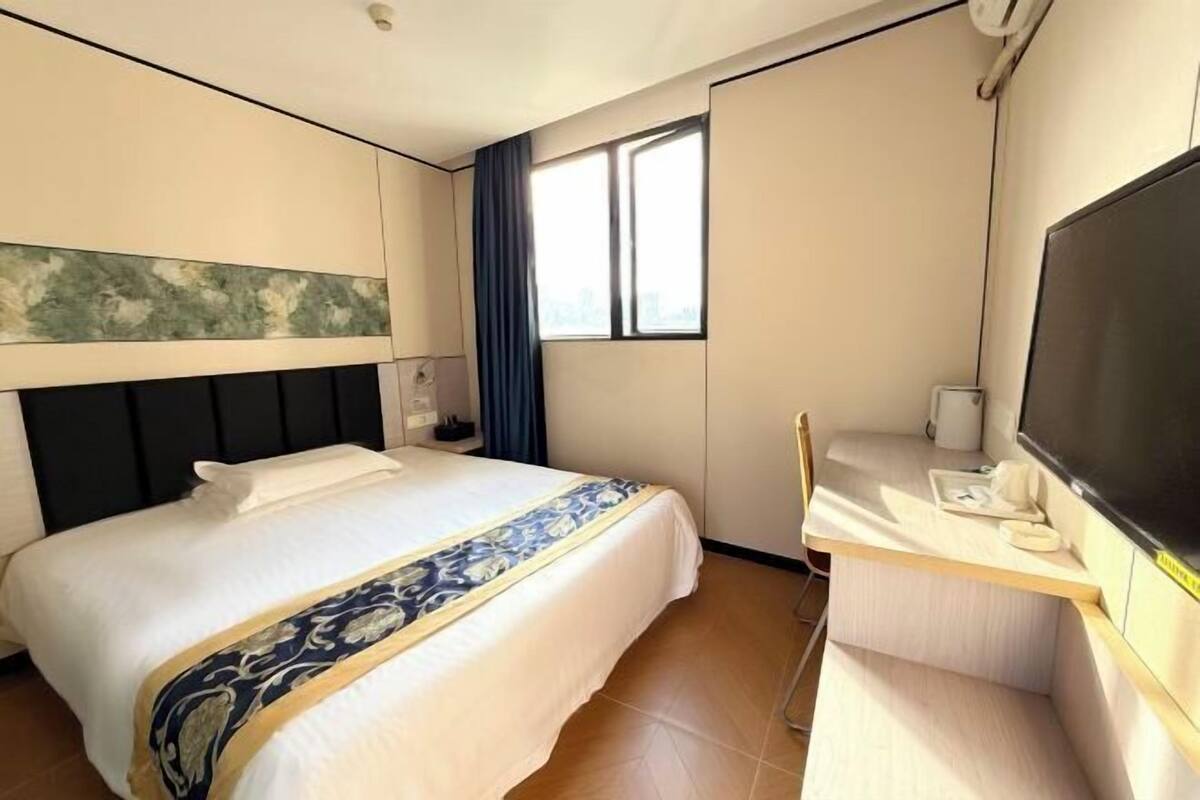 A hotel room with a bed, a desk with a chair, a television, and a window with curtains.