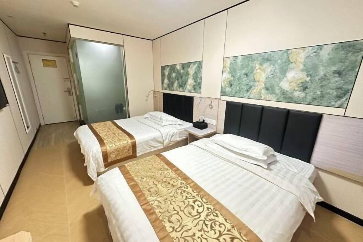 A hotel room with two beds, a large window with abstract art, a bedside table, and a door.