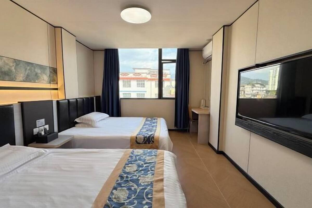 A hotel room with two beds, a TV, a desk, and a window with a city view.