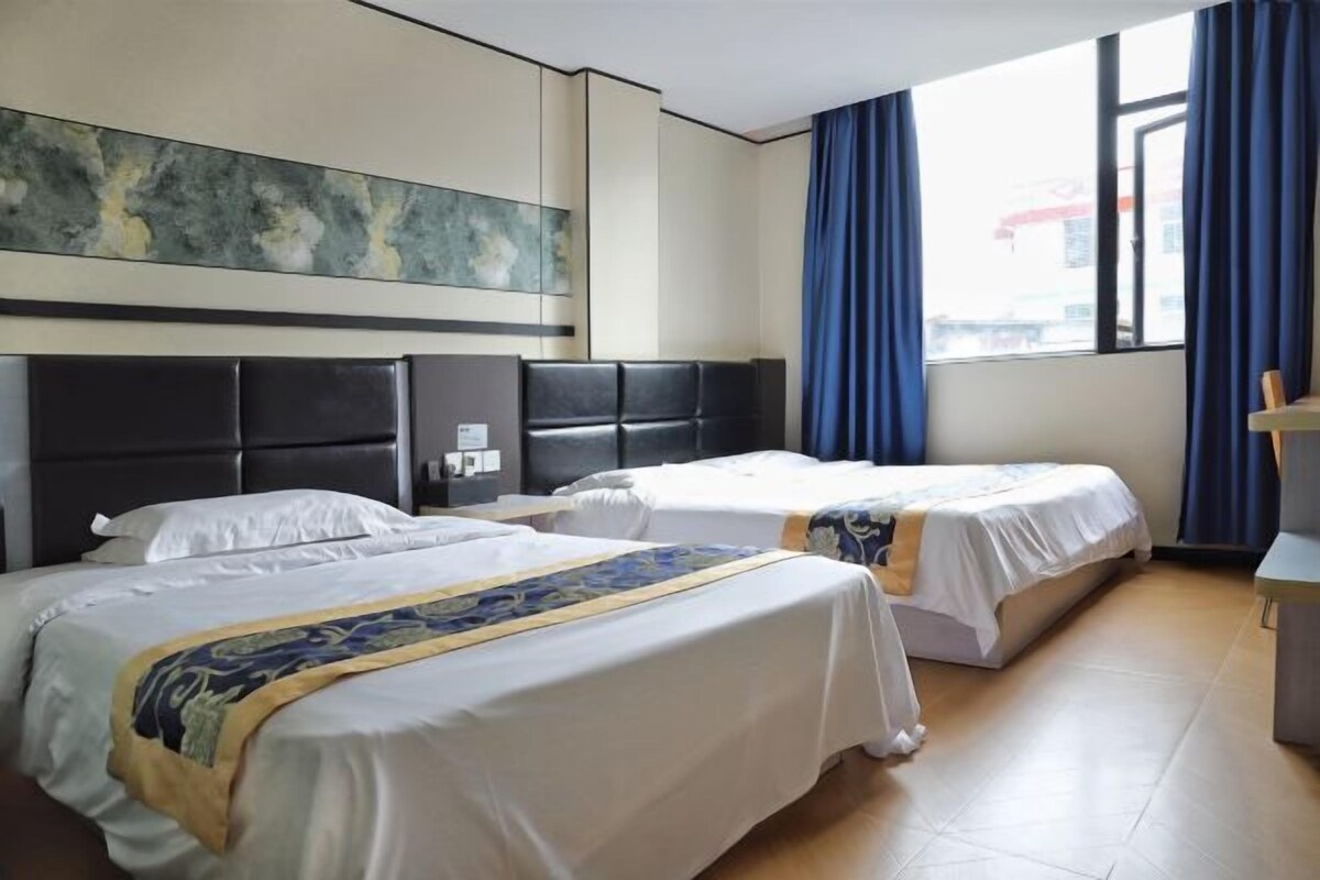 Une chambre d’hôtel avec deux lits, un grand tableau abstrait accroché au mur et une vue sur l’extérieur par une fenêtre ornée de rideaux bleus.