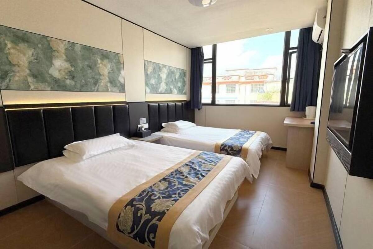 A hotel room with two beds, a large window, a flat-screen TV, and a wall-mounted artwork.