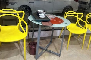 A small round table with a glass top, surrounded by four yellow chairs.