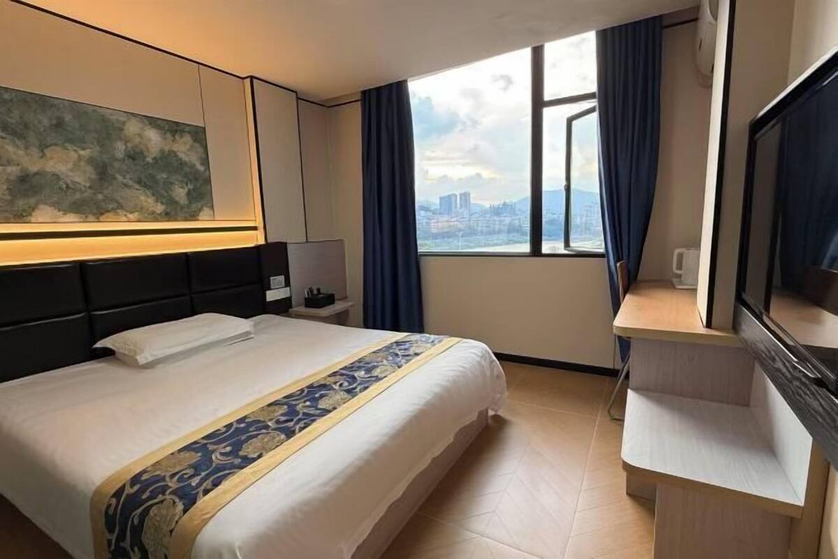 A hotel room with a large bed, a desk, a TV, and a window with a city view.