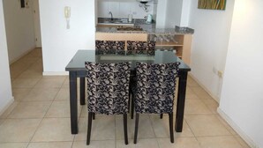 A dining area with a glass table and patterned chairs, a kitchen in the background, and a modern pendant light. - Exclusive Loft in Cordoba river view - 22B (Córdoba)