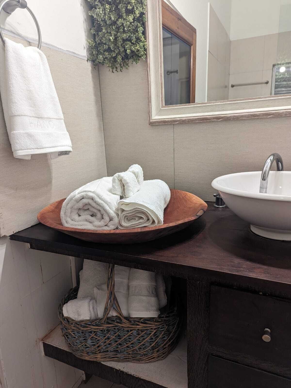 Un baño con lavabo, espejo, toallero y una cesta debajo del mueble.